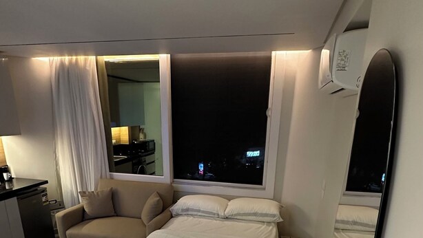Ett modernt hotellrum med en stor säng, en soffa, ett skrivbord och utsikt över staden på natten.