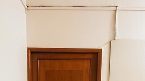 Une porte en bois dotée d’un clavier pour le verrouillage, située dans un coin, avec un sol carrelé et un mur aux couleurs blanc et beige.