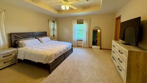 A bedroom with a bed, a nightstand, a dresser, a television, and a ceiling fan.