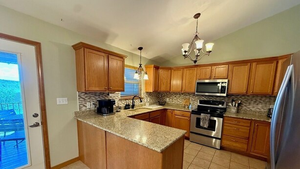 A kitchen with wooden cabinets, granite countertops, stainless steel appliances, and a chandelier.