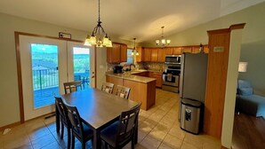 A modern kitchen with a dining area, large windows, and a view of the outdoors.