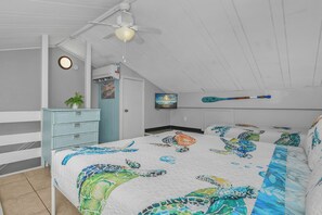 A bedroom with a bed, a dresser, a ceiling fan, a wall-mounted TV, and a door with a sign.