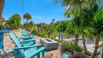 Outdoor seating with chairs and a fire pit, surrounded by palm trees and a water body.