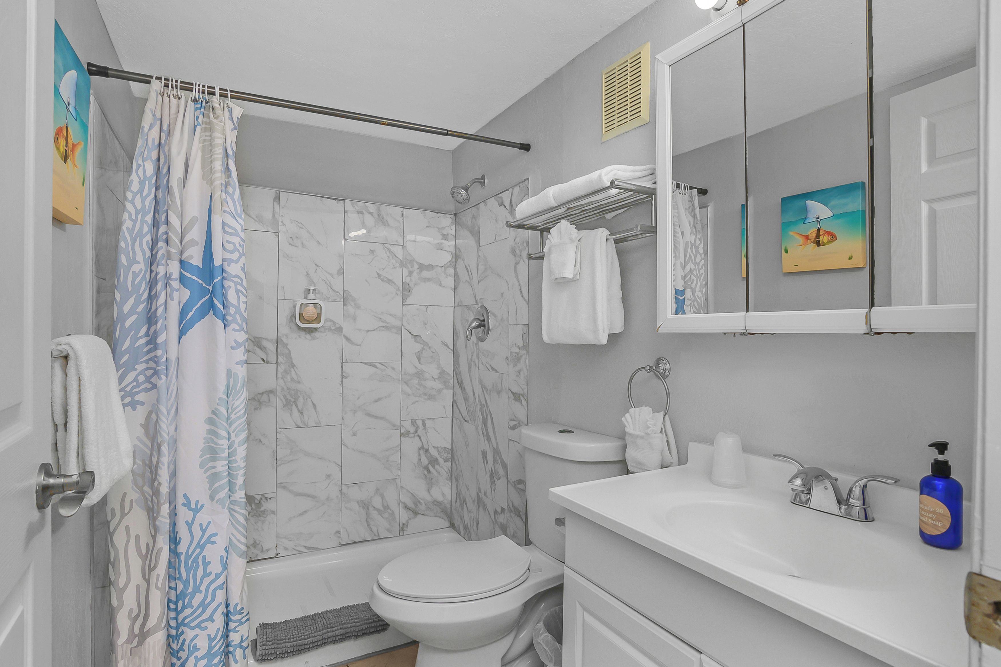 A bathroom with a shower curtain, a toilet, a sink with a soap dispenser, and a mirror.