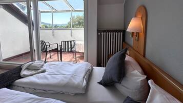 Een hotelkamer met een bed, nachtkastje, lamp, raam en uitzicht op de omgeving.