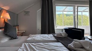 Une chambre d’hôtel avec un grand lit, un bureau, une lampe et une vue sur la verdure par la fenêtre.