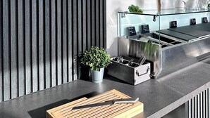Une cuisine moderne avec une planche à découper en bois, un couteau, une plante en pot, un évier en acier inoxydable et une horloge murale.