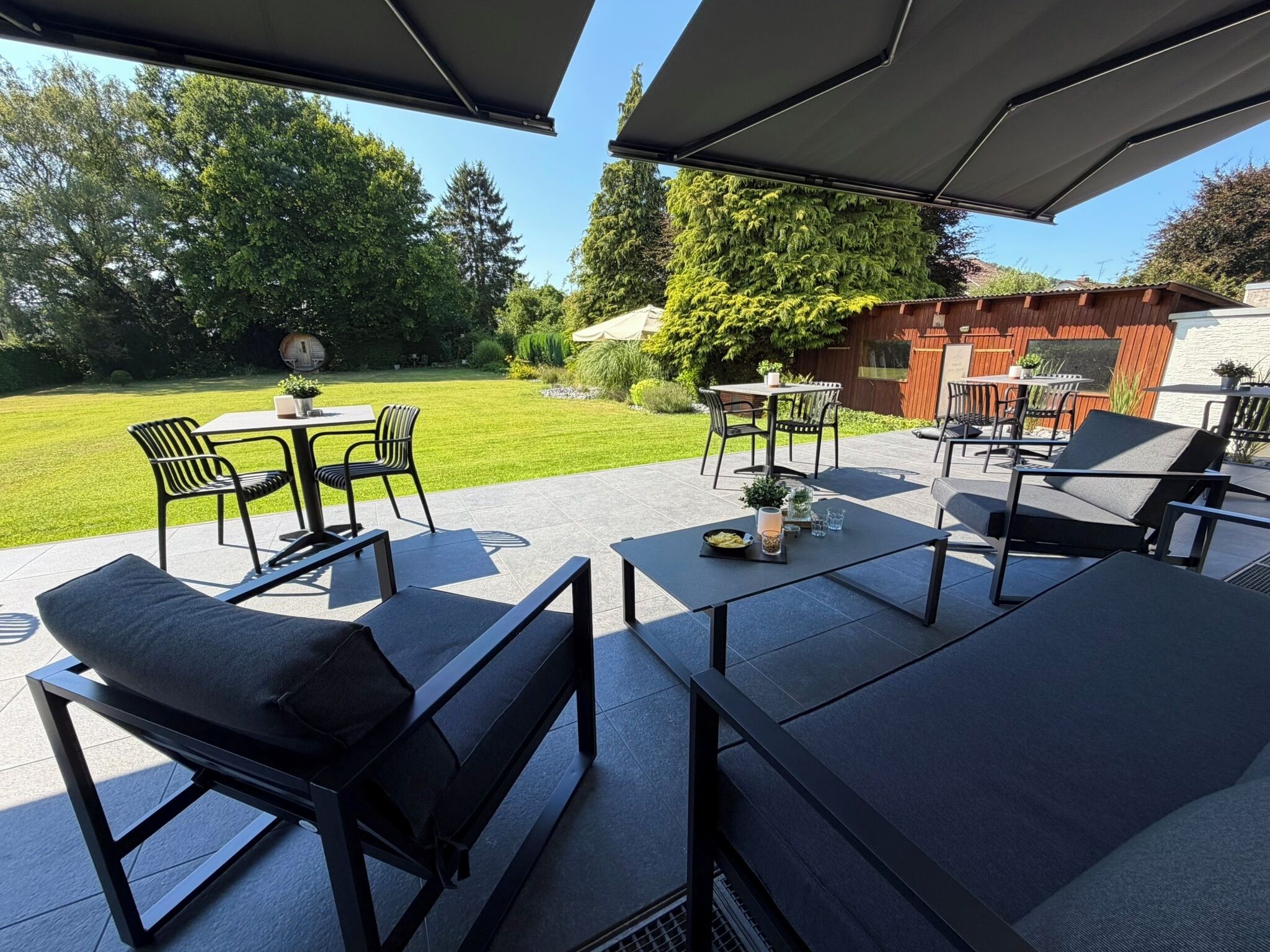 An outdoor patio area with modern furniture, including black chairs and tables, and a view of a well-maintained lawn and trees.