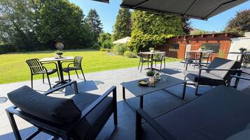 An outdoor patio area with modern furniture, including black chairs and tables, and a view of a well-maintained lawn and trees.