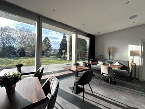 Una sala de estar moderna con comedor, ventanas amplias y vista a un jardín.