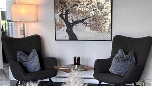 Un salon moderne avec deux fauteuils noirs, une lampe blanche, un grand tableau abstrait et un tapis en fourrure.