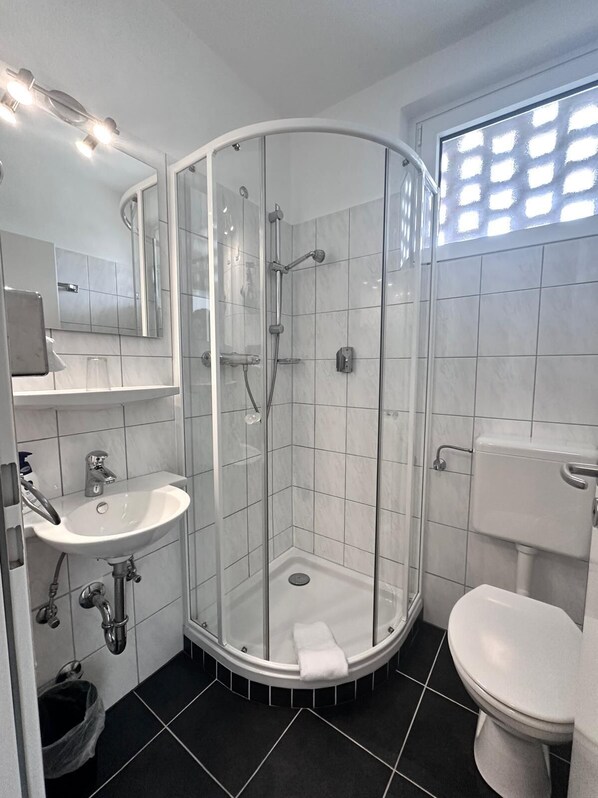 A modern bathroom with a glass-enclosed shower, a white sink, and a toilet. - Hotel Bevertal (Beverungen)