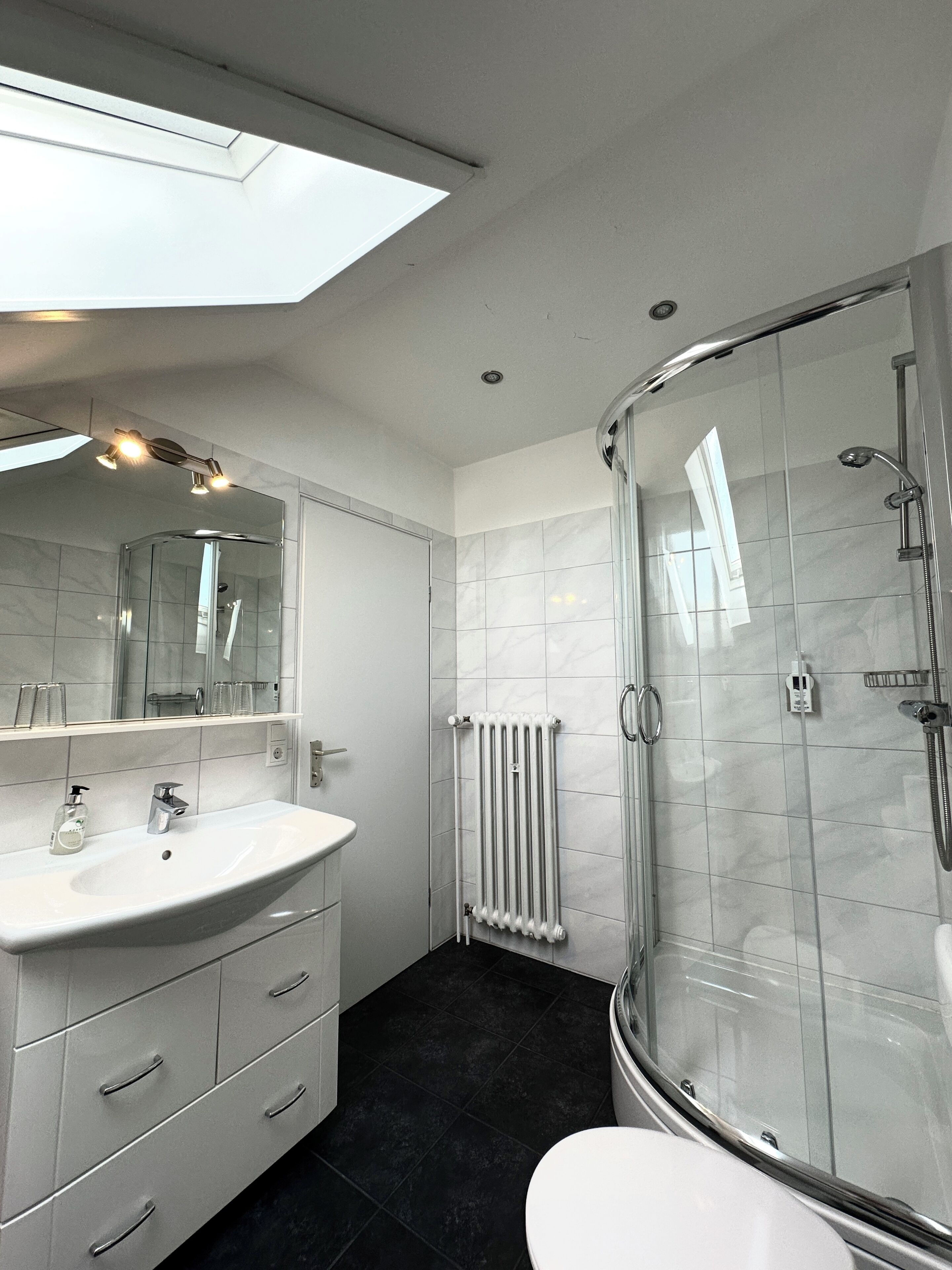 Une salle de bain moderne avec une douche à parois de verre, un lavabo blanc et un grand miroir.