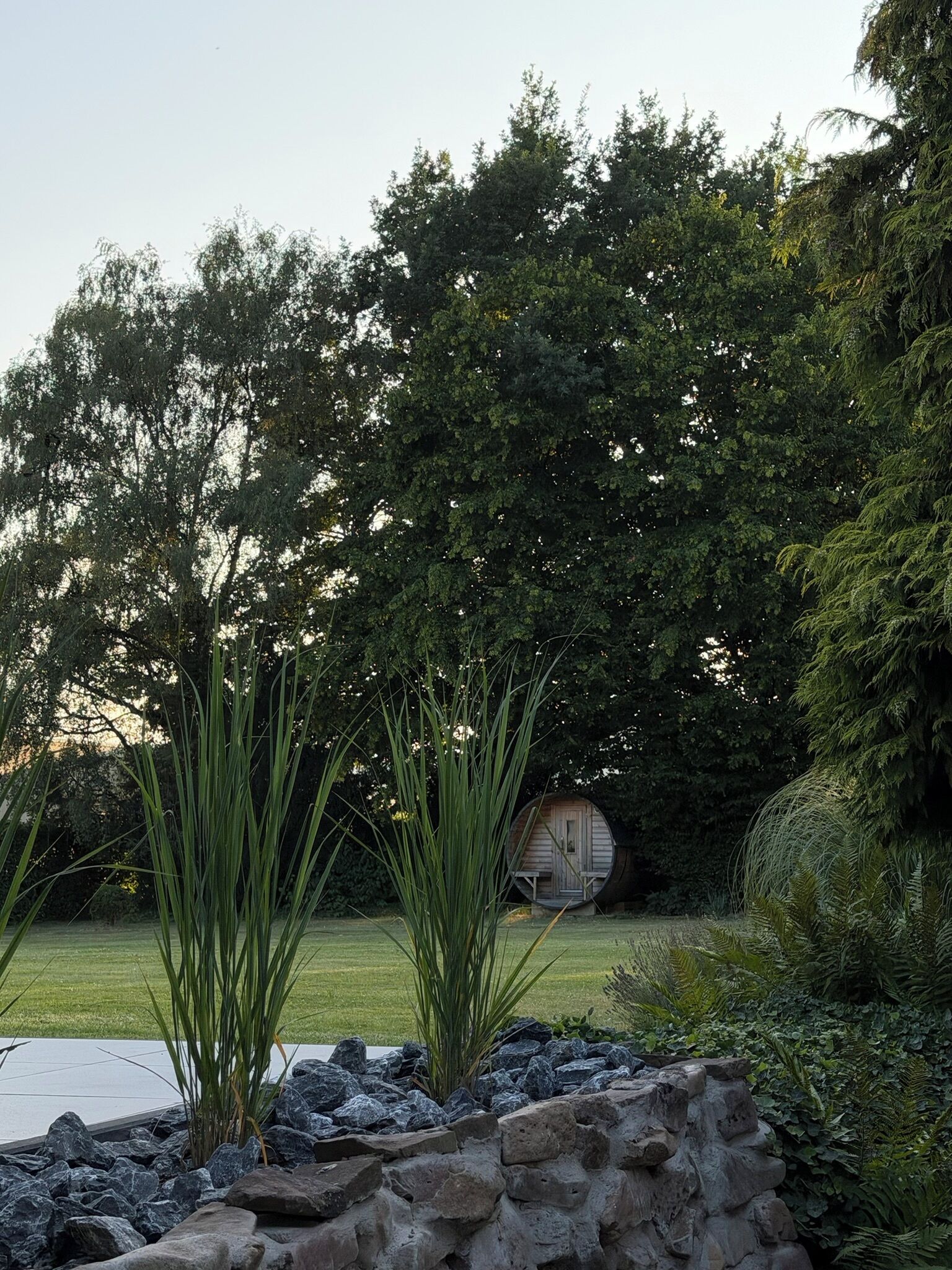 A garden with a stone wall, a wooden structure, and dense foliage.
