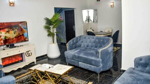 A modern living room with a TV, a sofa, a coffee table, and a potted plant. - Slim Anyaiwe Apartments (Agbor)