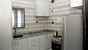 A kitchen with white cabinets, a window, a sink, a stove, and a refrigerator. - Slim Anyaiwe Apartments (Agbor)