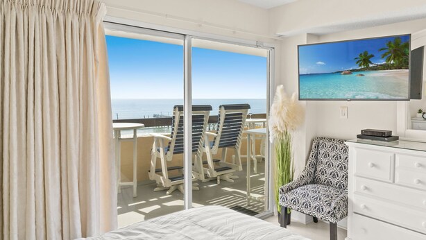 A hotel room with a balcony, a bed, a TV, and a chair. - Pristine Direct Oceanfront Getaway Luxury Oasis (North Myrtle Beach)