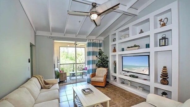 A living room with a white sofa, a coffee table, a TV on a white stand, and a ceiling fan. - Reserve.....Reserve Way (Naples)