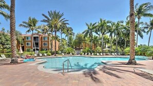 A pool area with palm trees, lounge chairs, and a building in the background. - Reserve.....Reserve Way (Naples)