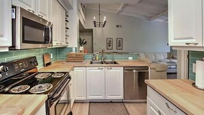 A modern kitchen with white cabinets, a black microwave, a stove, and a sink. - Reserve.....Reserve Way (Naples)