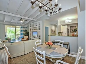A modern living room with a dining area, a ceiling fan, a TV, and a view of the outdoors.