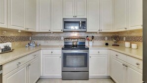 A kitchen with white cabinets, a stainless steel oven, a microwave, and a tiled backsplash. - Beautiful first floor Condo in gated community on private Davis Love golf course (Alva)
