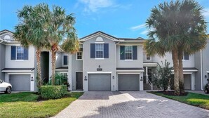 A modern two-story townhouse with a brick driveway, palm trees, and a garage. - Beautiful first floor Condo in gated community on private Davis Love golf course (Alva)