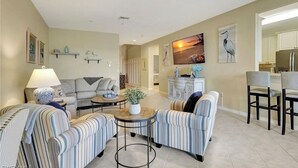 A living room with striped armchairs, a sofa, a coffee table, and a TV. - Beautiful first floor Condo in gated community on private Davis Love golf course (Alva)