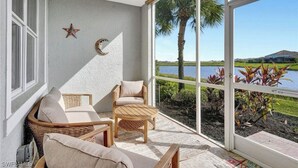 A balcony with wicker furniture, a star and crescent decoration, and a view of a lake and palm trees. - Beautiful first floor Condo in gated community on private Davis Love golf course (Alva)