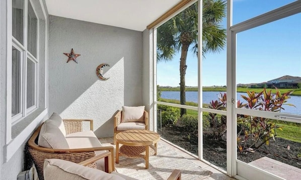 A balcony with wicker furniture, a star decoration, and a view of a lake and palm trees. - Beautiful first floor Condo in gated community on private Davis Love golf course (Alva)