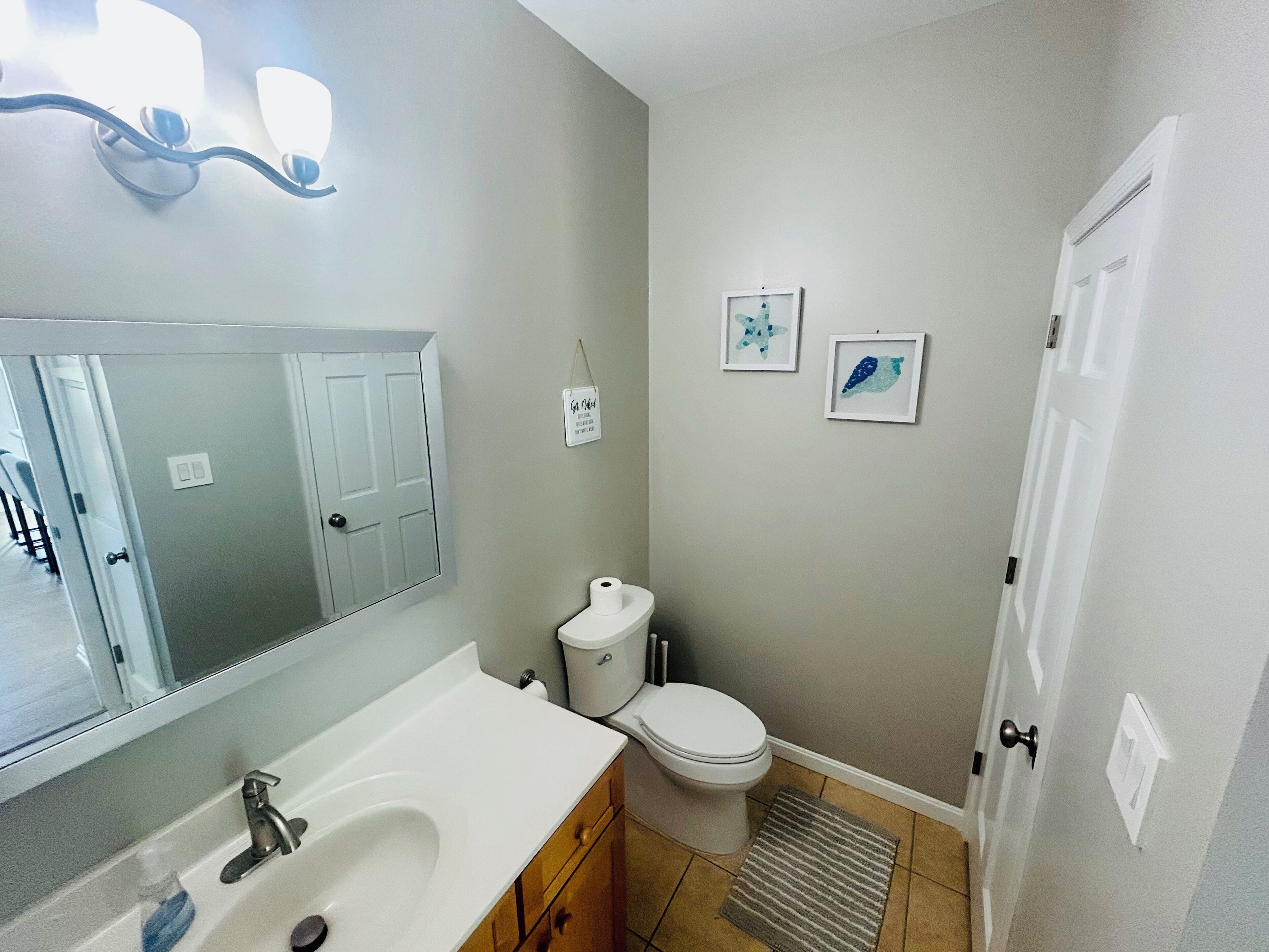 A bathroom with a white sink, mirror, toilet, and framed artwork on the wall.