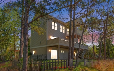 A two-story house with a balcony, surrounded by trees and a wooden fence.