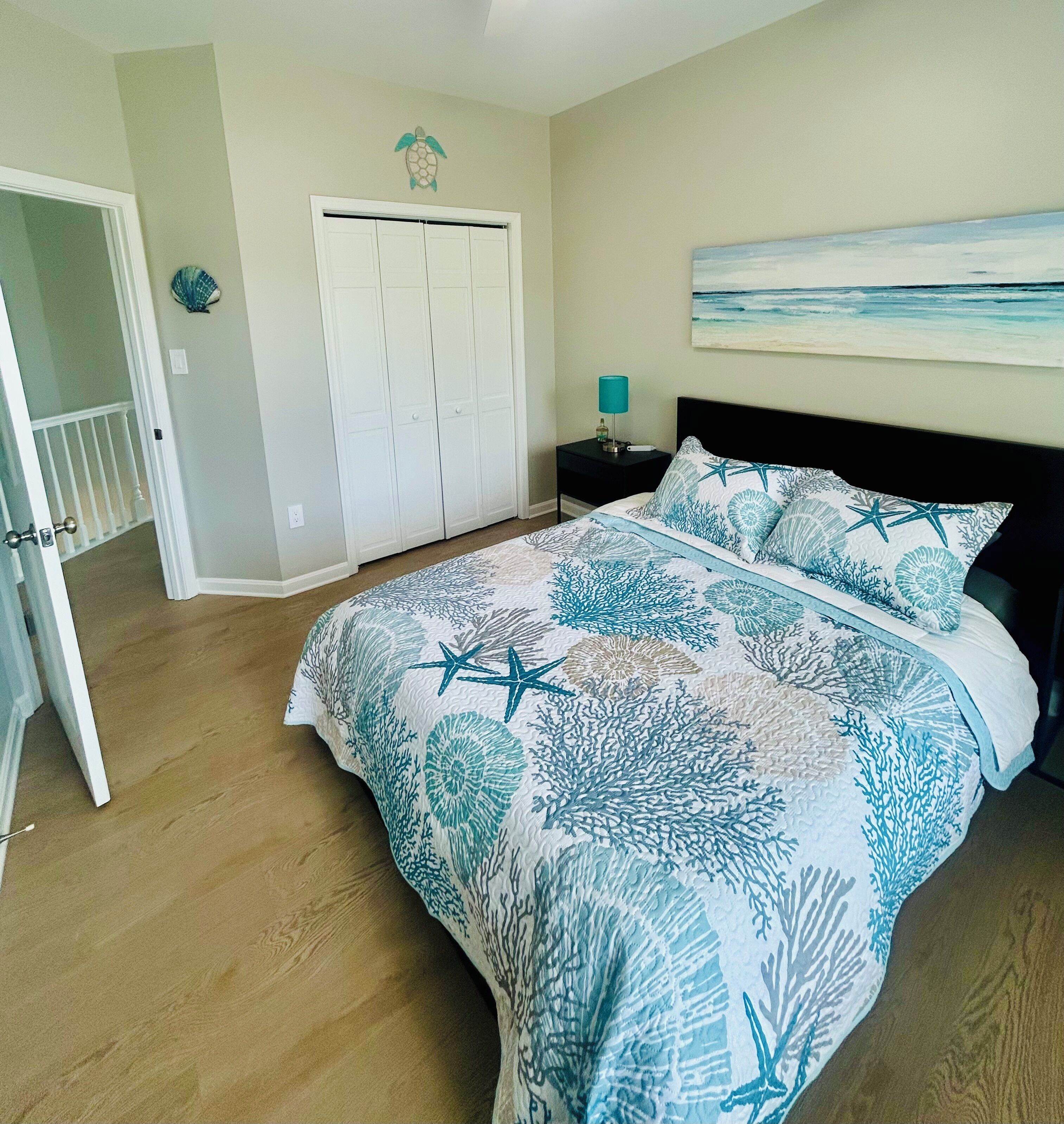 A bedroom with a bed, a nightstand, a door, and a wall with a painting.