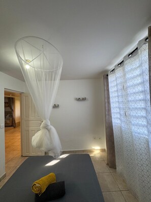A room with a bed, a white canopy, a small shelf, and a patterned curtain. - Maison du plateau - Horizon Caraïbes (Vieux-Habitants)
