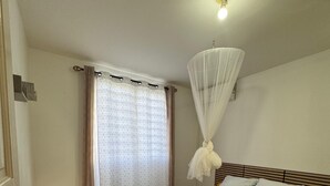 Een slaapkamer met een bed, gordijnen, een plafondlamp en een betegelde vloer.