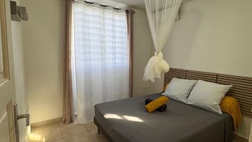 Une chambre à coucher avec un lit, des rideaux, un luminaire au plafond et un sol carrelé.