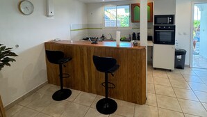 Een keuken met een houten keukeneiland, twee zwarte barkrukken, een magnetron en een spoelbak.