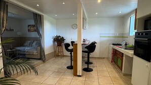 Een moderne keuken met witte kastjes, een fornuis en zwarte stoelen. Er staan potplanten en er is een eethoek met een tafel en stoelen.