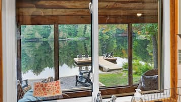 A cabin with a large window overlooking a lake and dock, wooden interior, and a view of the surrounding forest.