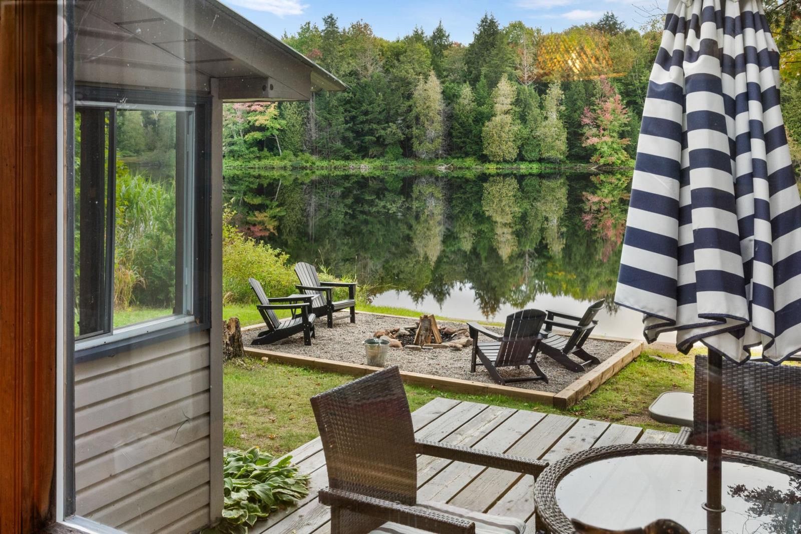 Järvenrantaterassi, jossa on Adirondack-tyylisiä tuoleja, pöytä ja raidallinen aurinkovarjo.