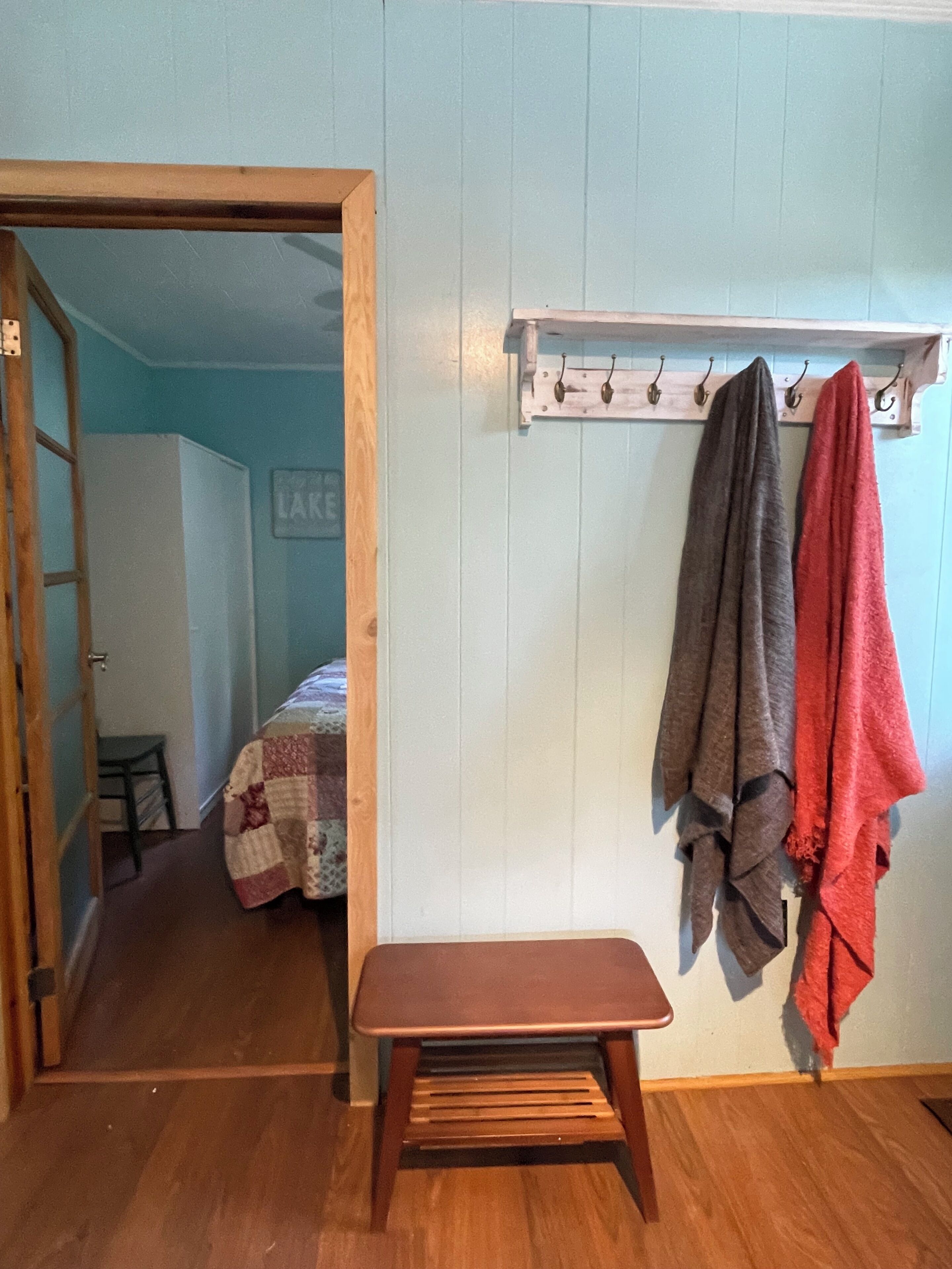 Ein Zimmer mit einer hölzernen Bank, einem Kleiderhaken mit zwei Handtüchern und einem Bett mit einer Bettdecke.