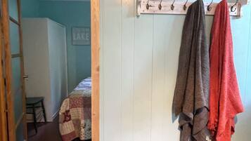 Ein Zimmer mit einer hölzernen Bank, einem Kleiderhaken mit zwei Handtüchern und einem Bett mit einer Bettdecke.