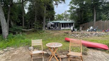 Ein Garten mit einem Holztisch und Stühlen, einem roten Kanu und einem Haus im Hintergrund.