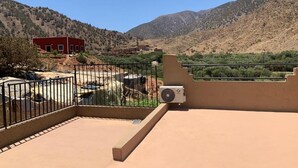 Una terraza en la azotea con vistas a un paisaje montañoso, un edificio rojo y un área cercada con materiales de construcción.