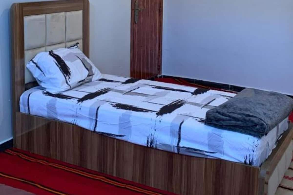 A single bed with a wooden headboard, a patterned bedspread, and a red carpet.
