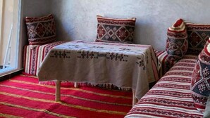 Una habitación con una cama cubierta de mantas estampadas, una mesita con mantel y una alfombra roja.