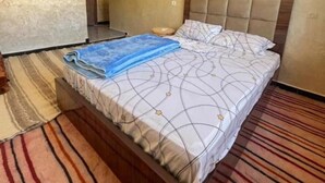 Una cama bien hecha con una colcha estampada, una manta azul y un cabecero de madera.