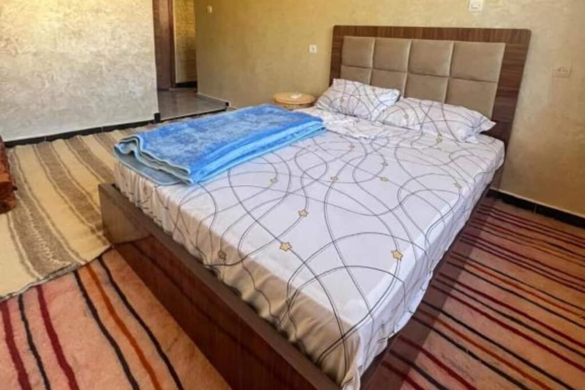 A neatly made bed with a patterned bedspread, a blue blanket, and a wooden headboard.