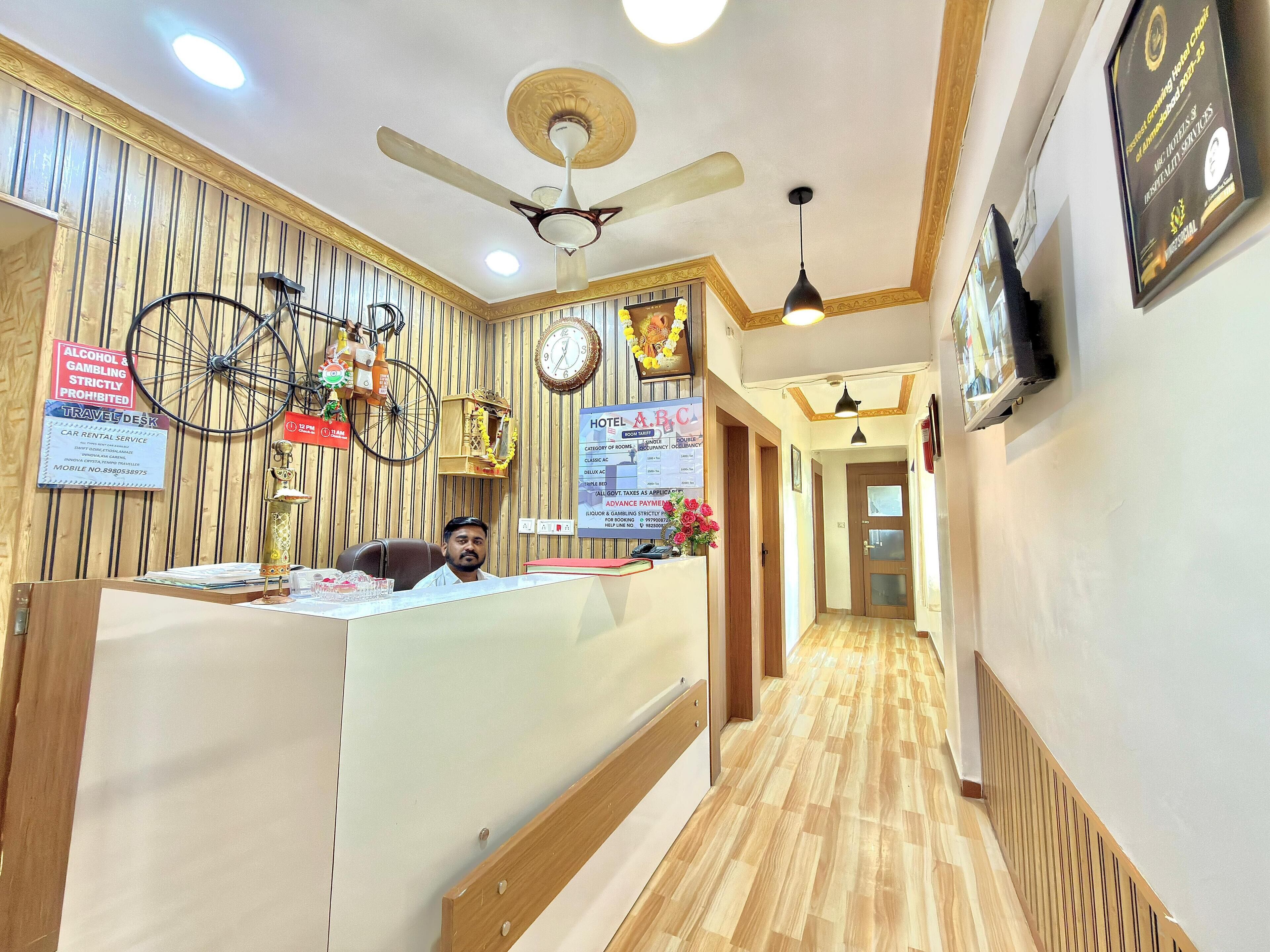 Zona de recepción de hotel con interior de madera, un mostrador de recepción, una bicicleta y varios carteles, incluyendo una política sobre la prohibición de alcohol y juegos de azar.