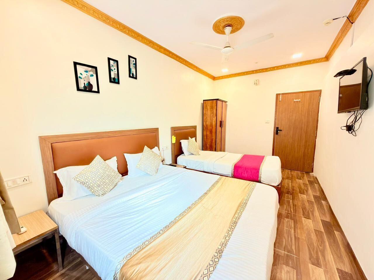 Habitación de hotel con dos camas, un armario de madera, un televisor en la pared y un ventilador de techo.